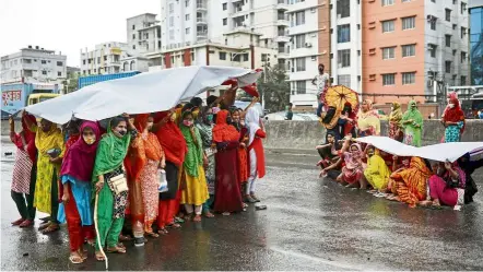  ?? — Reuters ?? Weathering adversity: Garment workers taking shelter from the rain under banners as they block a road in Dhaka to demand for their wages.