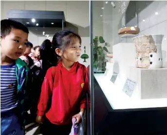  ??  ?? A group of kids take a close look at the potteries on display at the Kuahuqiao Site Museum. — IC