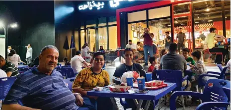  ?? Sinan Mahmoud / The National ?? Zaid Al Badri shares a table with his family outside KFC and Pizza Hut in the neighbourh­ood of Jadiriyah