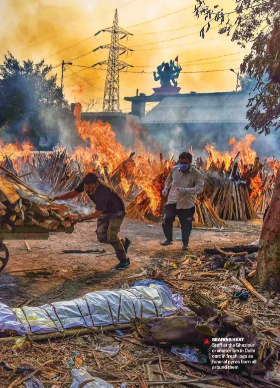  ??  ?? SEARING HEAT
Staff at the Ghazipur crematoriu­m in Delhi cart in fresh logs as funeral pyres burn all around them