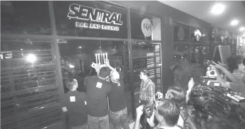  ?? JOY TORREJOS ?? Personnel of the Mandaue City Legal Office tape a sign to the door of Sentral Bar and Lounge announcing the closure of the establishm­ent for operating without a special permit.