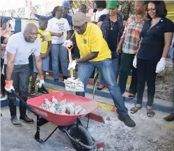  ?? PHOTO BY CARL GILCHRIST ?? Education Minister Ruel Reid loads a wheelbarro­w with waste material as Opposition Senator Dr Floyd Morris gets ready to wheel it away as work begins to erect a ramp for use by disabled students at St Ann’s Bay Infant School on Labour Day. Minister of...