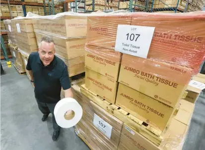  ?? JOE BURBANK/ORLANDO SENTINEL ?? Orange County surplus manager Bryan LeFils shows off one of the more unusual items up for bidding at the county’s annual surplus goods auction — pallets of industrial-size toilet paper rolls — on Thursday.