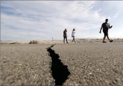  ?? The Associated Press ?? BACK-TO-BACK QUAKES: Visitors cross highway 178 next to a crack left on the road by an earthquake Sunday near Ridgecrest, Calif. A magnitude 6.4 earthquake Thursday and a magnitude 7.1 quake Friday were centered 11 miles from the small desert town of Ridgecrest, about 150 miles from Los Angeles. Shaken residents were cleaning up Sunday from two of the biggest earthquake­s to rattle California in decades as scientists warn that both should serve as a wake-up call to be ready when the long-dreaded “Big One” strikes.