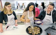  ??  ?? Kayleigh Mille, left, and Ella Music, right, look on as Kayla Todd spread glaze over cinnamon rolls during a molecular gastronomy class in the Carlow University food lab.