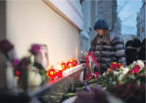  ?? ALEXANDER UTKIN / AFP / GETTY IMAGES ?? A woman lights a candle at the home stage building of the Alexandrov Ensemble (The Red Army Choir), in Moscow, on Sunday after a Russian military plane, which included dozens of Red Army Choir members, crashed on its way to Syria. There were no signs...