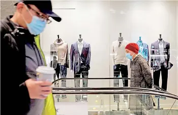  ?? — AFP photos ?? People wearing facemasks pass by a men’s clothing store at The Shops at Columbus Circle in New York.