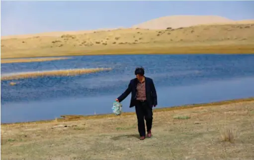  ??  ?? A local environmen­tal volunteer picks up a plastic bag from a lake at an attitude of 3,200 meters in Qinghai Province. VCG