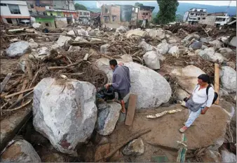  ?? JAIME SALDARRIAG­A / REUTERS ?? People walk on a street destroyed after flooding and mudslides caused by heavy rains, which led several rivers to overflow, pushing sediment and rocks into buildings and roads, in Mocoa, Colombia on Sunday.