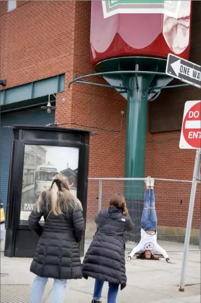  ?? Tim Robbibaro/For the Post-Gazette ?? Terri Nardi, 65, of Baden, does a headstand for her family Saturday beneath the newly installed Heinz ketchup bottle at the Senator John Heinz History Center in the Strip District.