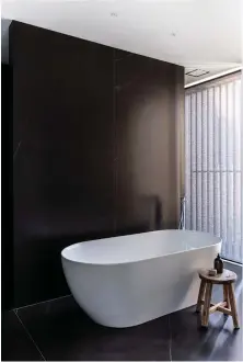  ??  ?? This page, top right
The master ensuite’s silk-finish Neolith Calatorao tiles and the continuati­on of the dark joinery highlight the freestandi­ng bath