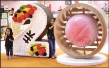  ?? CHINA DAILY PARKER ZHENG / ?? Two girls pose with a “20” statue in the shapes of a richly decorated birthday cake and Chinese birthday bun, marking the 20th anniversar­y of Hong Kong’s return to the motherland, at a shopping mall in Po Lam.