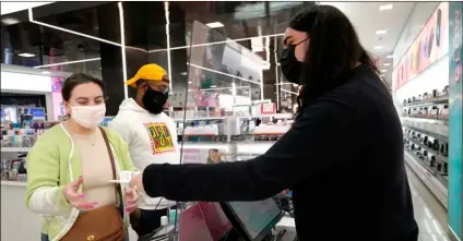  ?? AP Photo/Charles Rex Arbogast ?? Cashier Druhan Parker (right) works behind a plexiglass shield on Nov. 19 as he checks out shoppers Cassie Howard (left) and Paris Black at an in Chicago.