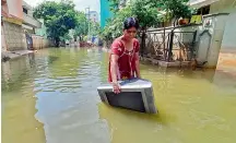  ?? —P.SURENDRA ?? A woman carries her household belongings through standing water in P&T Colony on Saturday. The water from Tuesday’s rains has still not been cleared in the area.