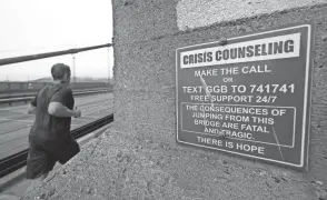  ?? ERIC RISBERG/AP FILE ?? A man jogs past a sign about crisis counseling on the Golden Gate Bridge in San Francisco in August.