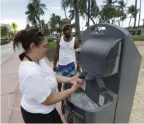  ?? Wilfredo Lee, The Associated Press ?? Maria Gomez, foreground, washes her hands at a portable hand washing station as she and Barry Molett, back, enjoy a day on Miami Beach on Monday.