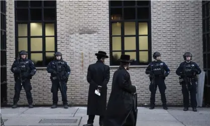  ??  ?? Orthodox Jewish men pass police guarding a Brooklyn synagogue prior to a funeral for a victim of the shooting inside a Jewish grocery, 11 December. Photograph: Mark Lennihan/AP