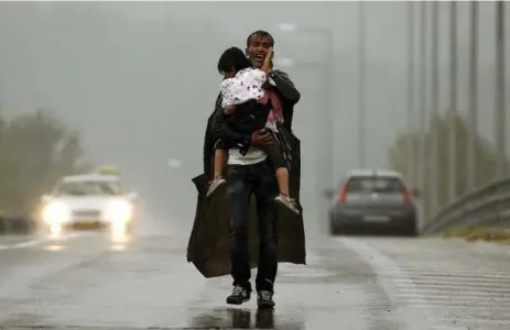  ?? YANNIS BEHRAKIS/REUTERS ?? A Syrian refugee shouts at others to wait for him as he carries his daughter through a rainstorm toward Greece’s border with Macedonia on Thursday.