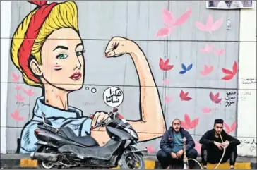  ?? AHMAD AL-RUBAYE/AFP ?? An Iraqi man smokes a water pipe under a feminist mural painting with the Arabic slogan ‘This is what our women are like!’ in Baghdad’s Tahrir Square on November 21.