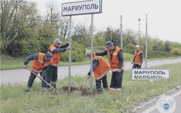  ?? ?? Municipal workers changing Ukrainian road signs to Russian outside the city of Mariupol