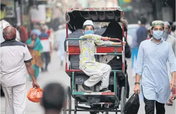  ??  ?? A boy wearing a protective face mask rides in a cycle rickshaw in the old quarter of Delhi.