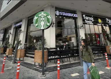  ?? (AP/Ali Abdul Hassan) ?? A woman walks by an unlicensed Starbucks cafe in Baghdad on Dec. 21. Real Starbucks merchandis­e is imported from neighborin­g countries to stock the three cafes in the city, but all are unlicensed.