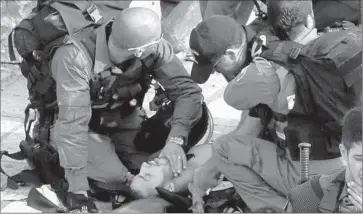  ?? Gali Tibbon AFP/Getty Images ?? ISRAELI BORDER GUARDS aid an injured police officer, one of two who were stabbed outside the Old City in East Jerusalem, the second such attack in the same area. The attack took place near the Damascus Gate.