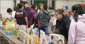  ?? FRAN MAYE - DIGITAL FIRST MEDIA ?? Parents look over an assortment of books and toys during the Christmas Basket program Saturday in New Garden.