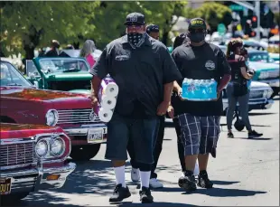  ??  ?? Mike Maes and his son Miguel Maes, both lowriders with the Tu Sabes Car Club, carry supplies brought by caravan from San Jose to help farmworker­s in Gilroy on Saturday.