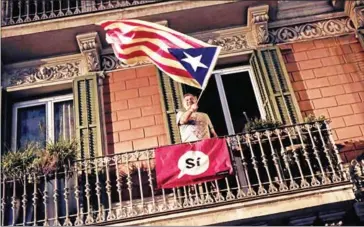  ?? PAU BARRENA/AFP ?? A man waves a pro-independen­ce Catalan flag from a balcony after the closing of the La Fontana youth centre polling station, on October 1, in Barcelona.