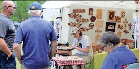  ?? / Diane Wagner ?? Tyler Wilson (center) looks up from his scroll saw in his grandfathe­r’s booth, Pop’s Shop, where he is cutting out wooden animals to give to children Sunday at the Cave Spring Arts Festival.