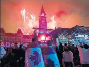  ?? CP PHOTO ?? People wearing Canadian flags watch fireworks explode over the Peace Tower during the evening ceremonies of Canada’s 150th anniversar­y of Confederat­ion, in Ottawa on Saturday.