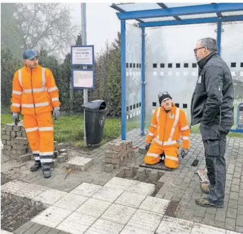  ?? FOTO: THOMAS ANNEN ?? David Heinz (links) und Meik Wack vom Bauhof Großrossel­n arbeiten an einer Bushaltest­elle im Ortsteil Naßweiler: Die geriffelte­n Betonstein­e, die als Orientieru­ng für sehbehinde­rte Menschen dienen, werden neu verlegt. Rechts Vorarbeite­r Jürgen Kneip.