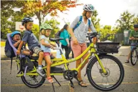  ?? JEFF WHEELER/MINNEAPOLI­S STAR TRIBUNE/TRIBUNE NEWS SERVICE ?? Stephanie Brodegard reaches for a water bottle after getting her three kids situated on her cargo bike after picking up her son Grant, 6, from school in Minneapoli­s. The other kids are Lewis, 1, and Darcy, 4.