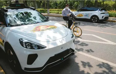  ?? NG HAN GUAN/AP ?? A bicyclist pedals last month down a Beijing street among self-driving taxis developed by Chinese tech giant Baidu Inc.