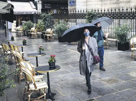  ??  ?? A couple of pedestrian­s wearing protective face masks walk past a deserted bistrot terrace, Paris, Sept. 25, 2020.