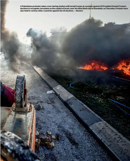  ?? Reuters ?? A Palestinia­n protester takes cover during clashes with Israeli troops at a protest against US President Donald Trump’s decision to recognise Jerusalem as the capital of Israel, near the West Bank city of Ramallah, on Thursday. Protests were also held...