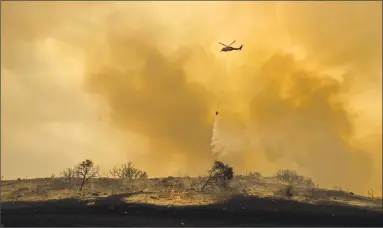  ?? Noah Berger / Associated Press ?? A helicopter drops water while trying to keep a wildfire from jumping Santa Ana Road near Ventura, Calif., on Saturday.