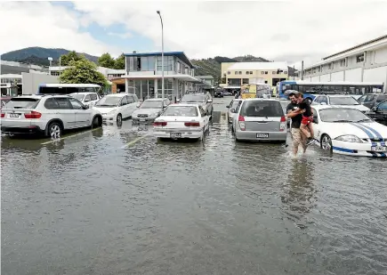  ?? MARTIN DE RUTYER/NELSON MAIL ?? A man carries his son through saltwater from the 4.5m king tide that overflowed in the Wakatu Square carpark.