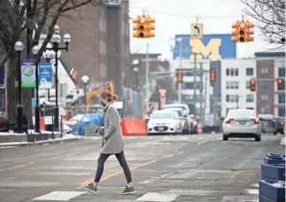  ?? MANDI WRIGHT/DFP ?? A pedestrian crosses the street in Ann Arbor on Monday. A new virus variant has been confirmed among at least 13 student athletes and shut down campus sports for two weeks.