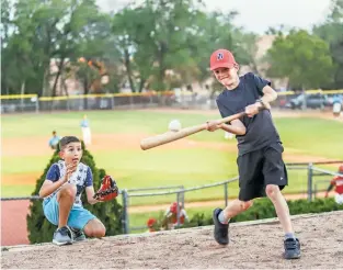  ?? GABRIELA CAMPOS/THE NEW MEXICAN ?? Greyson Fritzmeier, 10, gets a solid hit while Zachary Bartak, 10, plays catcher above Fort Marcy Ballpark while the Santa Fe Fuego play below Thursday evening in their season opener against the Alpine Cowboys.