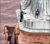  ?? PIX11 ?? A person leans against the robes of the Statue of Liberty as a police officer climbs a ladder to stand on a ledge nearby to talk the climber into descending.