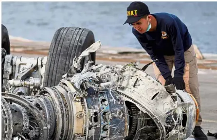  ??  ?? Tragic scenes: ( Top) An Indonesian National Transporta­tion Safety Commission official examining a turbine engine at Tanjung Priok port in Jakarta while (left) a woman, whose husband was on the Lion Air flight, cries as she holds their son after a news conference.