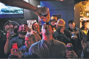  ??  ?? Jack Choate accepts a free shot from bar owner Carey Suckow in the party atmosphere on Tuesday night when the landmark neon sign lit up San Francisco’s Mission District again.