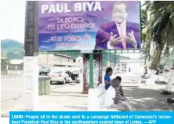  ??  ?? LIMBE: People sit in the shade next to a campaign billboard of Cameroon’s incumbent President Paul Biya in the southweste­rn coastal town of Limbe. —AFP