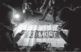  ?? KIRAN RIDLEY/GETTY ?? People on Thursday in Calais, France, place candles on the edges of a banner that translates to “309 dead on the France/UK Border since 1999.”