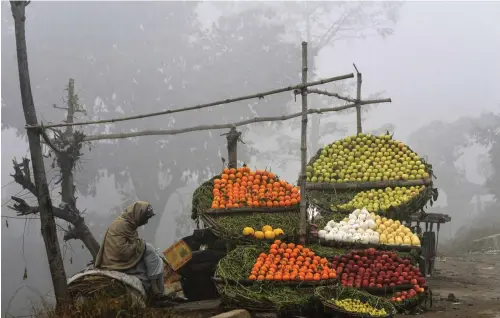  ?? — AFP ?? A vendor waits for customers at a streetside stall during heavy fog in Lahore, on Wednesday.