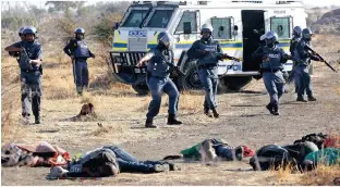  ??  ?? LINE OF FIRE: Policemen in front of some of the dead miners after they were shot in Marikana on August 16, 2012. The police had opened fire on striking miners armed with machetes and sticks at Lonmin’s Marikana platinum mine, leaving several corpses...