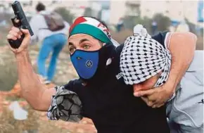  ??  ?? An Israeli undercover policeman wielding a pistol while grabbing a Palestinia­n protester in Ramallah on Friday.