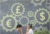  ??  ?? Chinese people walk by a mural displaying world currency symbols outside a bank in Beijing on Monday.